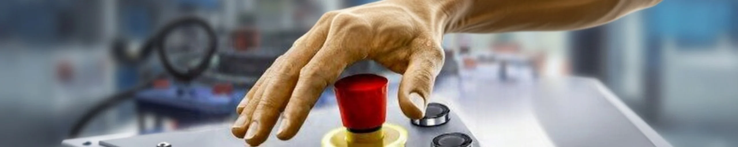 Close-up of a hand pressing a red industrial emergency stop button on a control panel, symbolizing machine safety and AS/NZS compliance.
